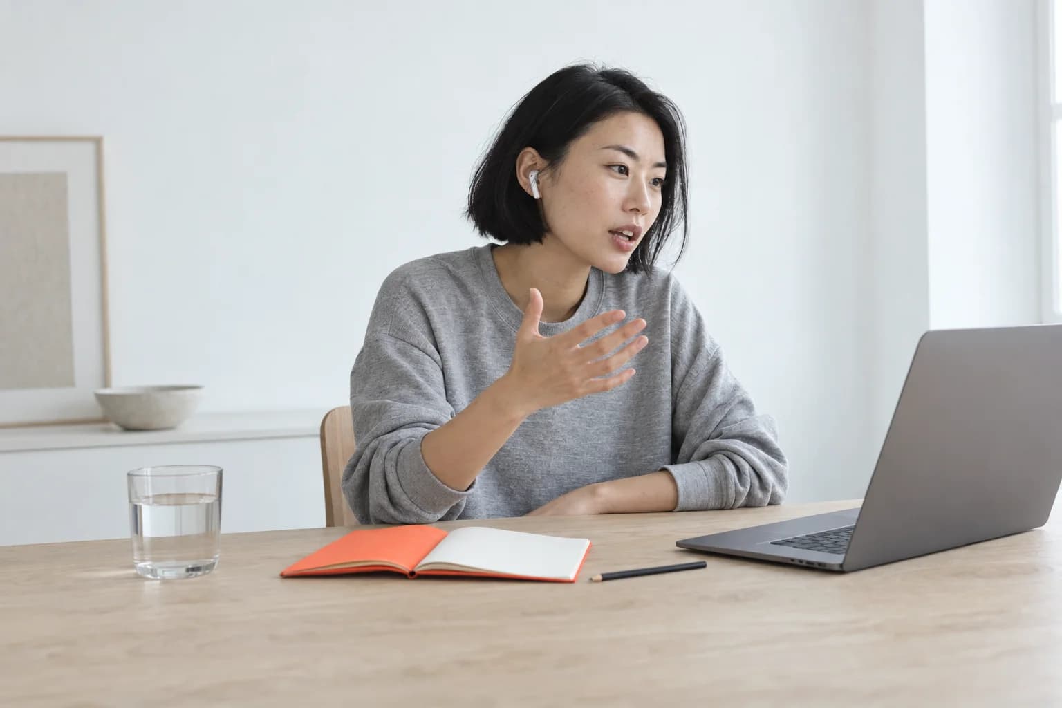 Wearing earbuds, she answers a question out loud at her laptop.